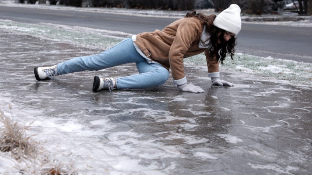 A young woman pushes herself up after slipping and falling on an icy sidewalk